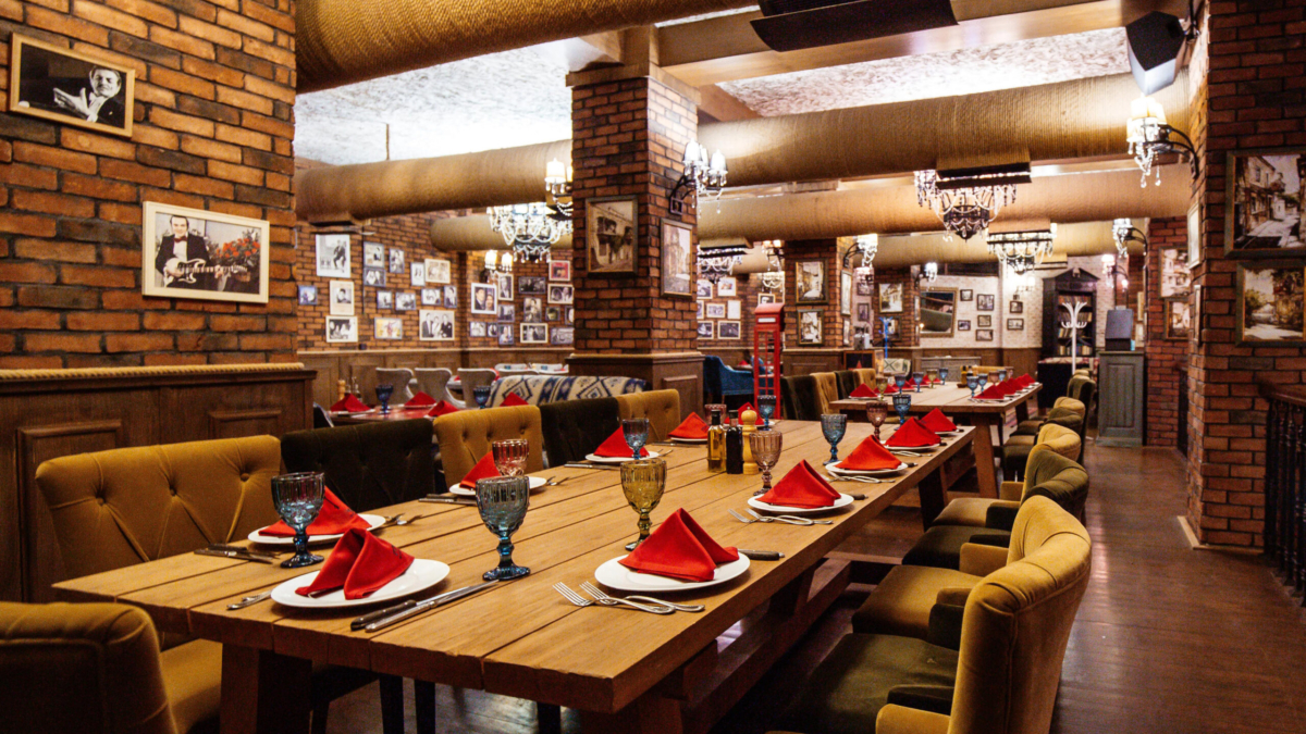 a restaurant hall with red brick walls wooden tables and pipes in the ceiling